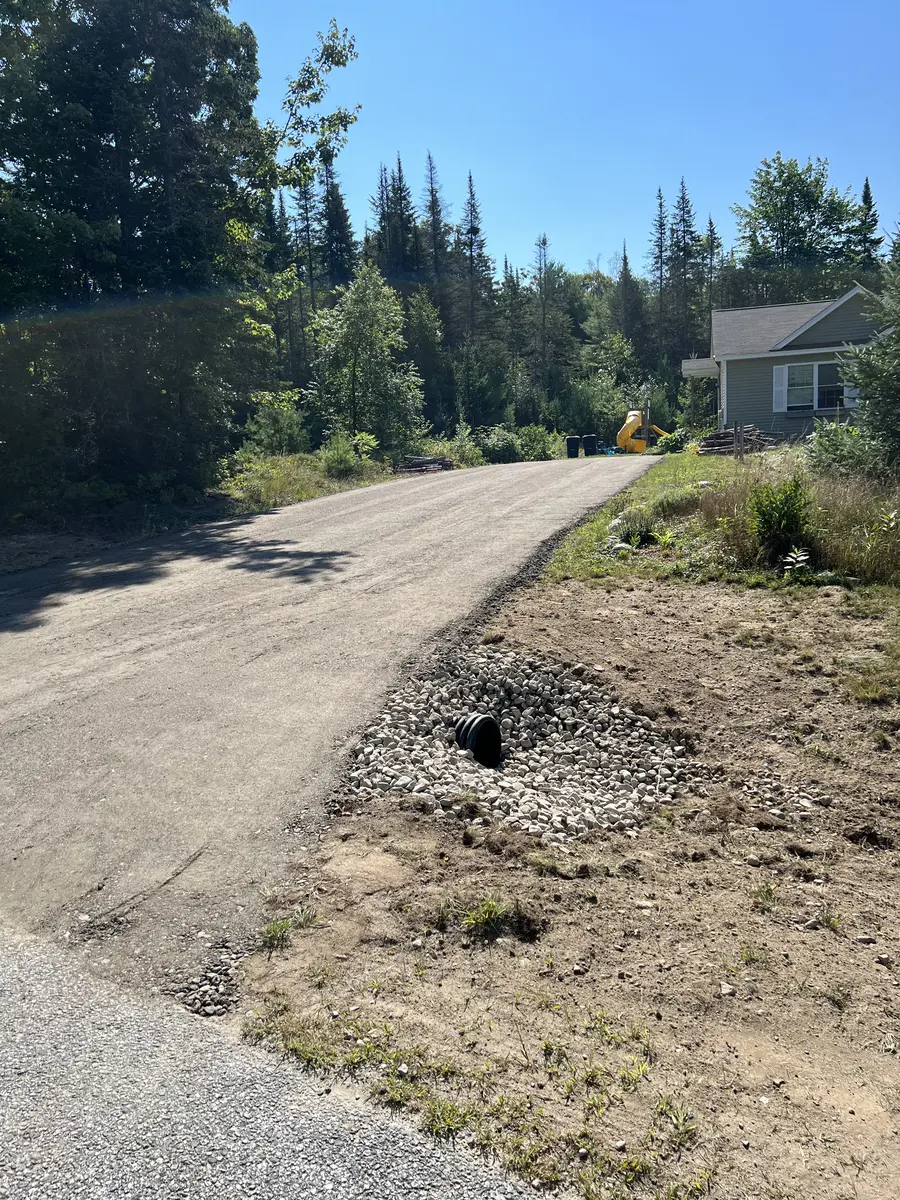 New gravel driveway curving through trees to a wooded house lot